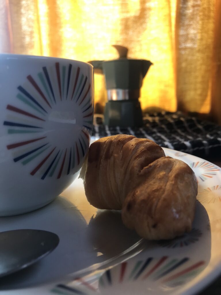 Taza de café, cafetera italiana y medialunas junto a la cortina amarilla